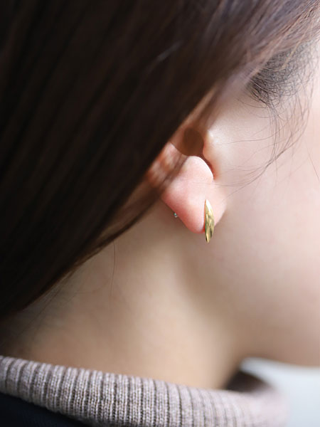 女性の耳元をアップで写し、ワイズマンピアスの立体感とK18コーティングの落ち着いた輝きが分かる着用画像。