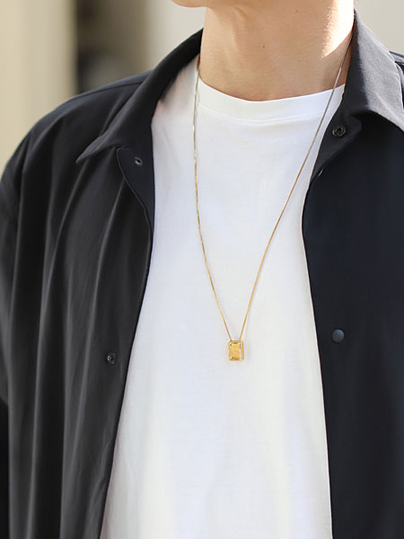 エスカプラーリオ ネックレスを男性がゴールド側を表にして着用し、胸元で落ち着いた輝きが映える画像。