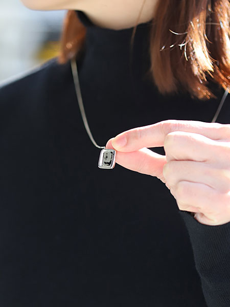 女性が指先でネックレストップをつまんで持ち、エスカプラーリオネックレスのトップの大きさや厚みが分かる画像。