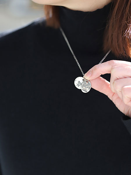 女性が指先でネックレストップをつまんで持ち、ダブルプレートの大きさや厚みと重なり具合が分かる画像。