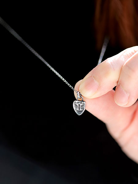 女性が指先でネックレストップをつまんで持ち、ピジョンチャームの大きさや立体感が分かるように写した画像。