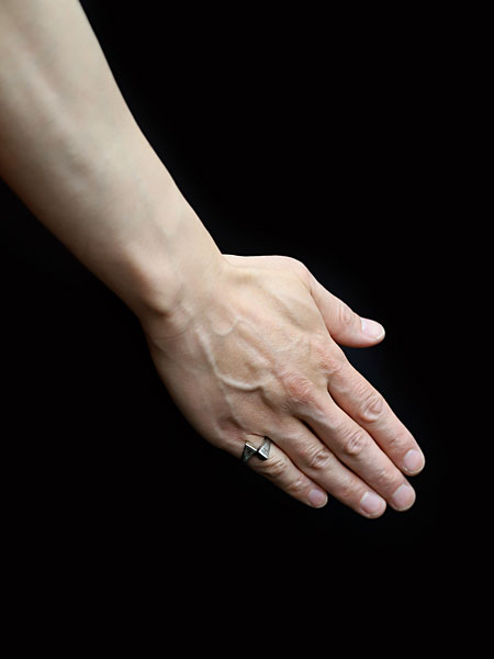 クロスデザインのシルバーリングをピンキーリングとして着用した男性の手元アップ画像。