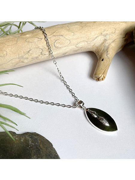 流木や観葉植物と並べて飾ったワニモチーフシルバーネックレス、自然を感じるディスプレイ画像。