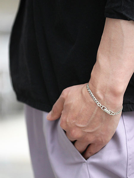 カーブチェーンブレスレットを男性が着用した横からのスタイリング画像で、手首にほどよい存在感を与える着用イメージ。