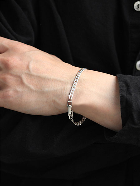 カーブチェーンブレスレットを男性が着用した手元アップの画像で、シンプルなコーデにも映える存在感がわかります。