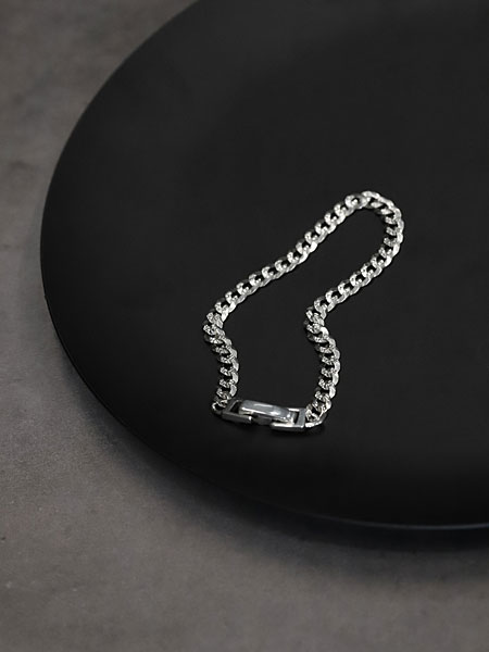 黒い丸い台の上に無造作に置いたカーブチェーンブレスレットのディスプレイ画像で、シルバーの質感と雰囲気が際立ちます。