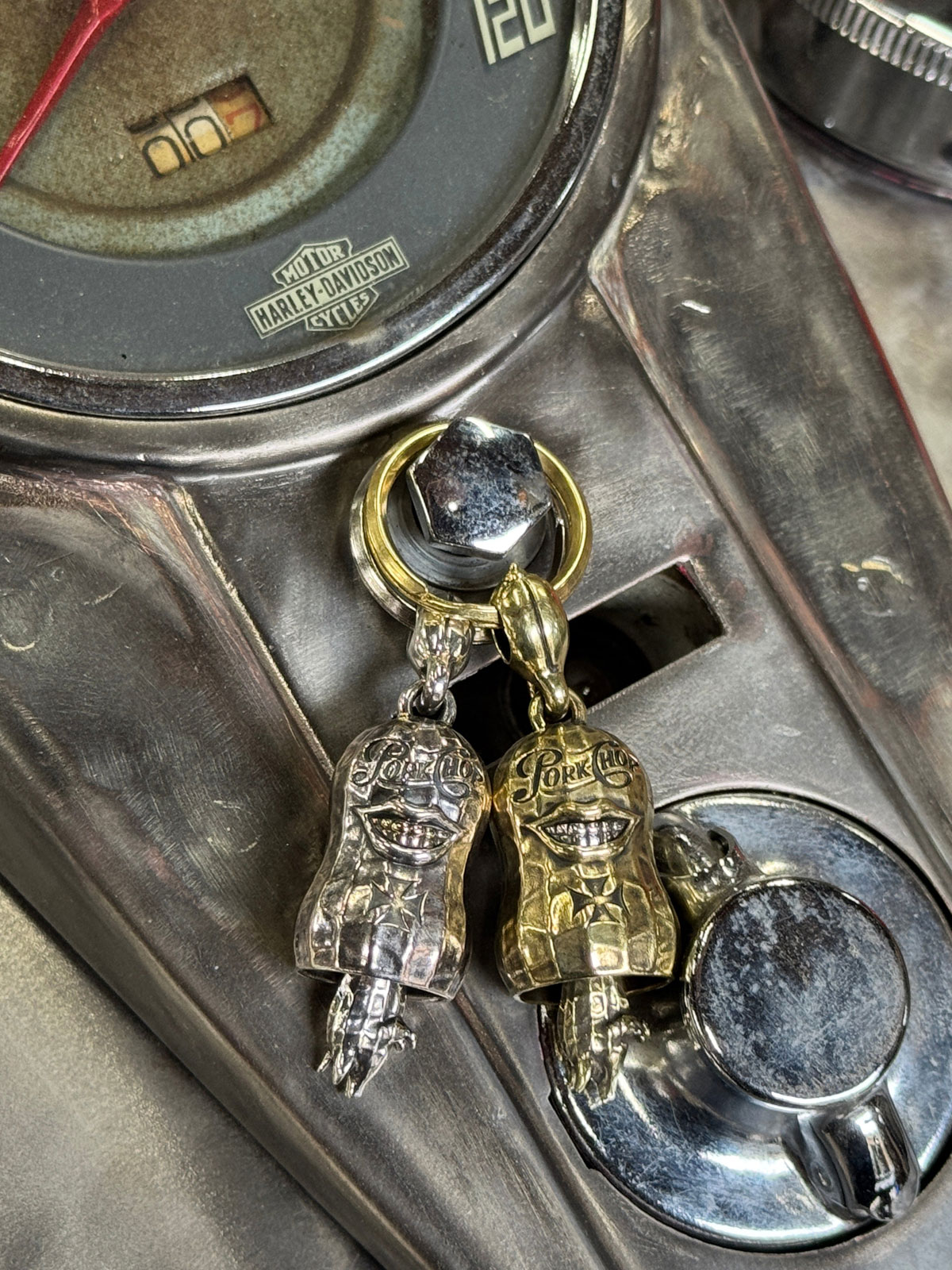 ハーレーのタンクの上にシルバーとブラスのガーディアンベルを並べて置いた質感の違いがわかる比較画像。