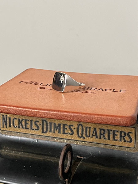 BELIEVEINMIRACLEの焼き印が入ったレザーの上にシグネットリングを置き、ブランドの世界観が伝わるイメージ画像。