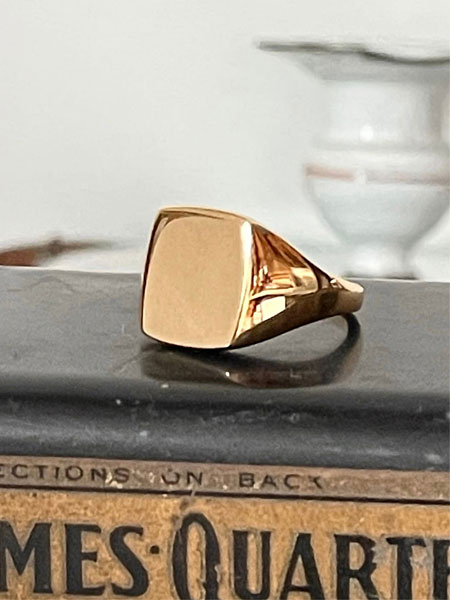 雰囲気のあるアメリカンな台の上に置かれたシグネットリングを斜め前から捉えた、立体感のあるディスプレイカット。