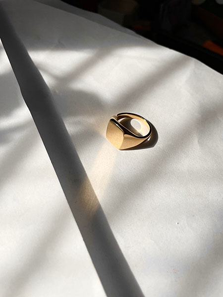 白い背景の上に置かれたシグネットリングで、ゴールドの色味とシンプルなフォルムが際立つクリーンな一枚。