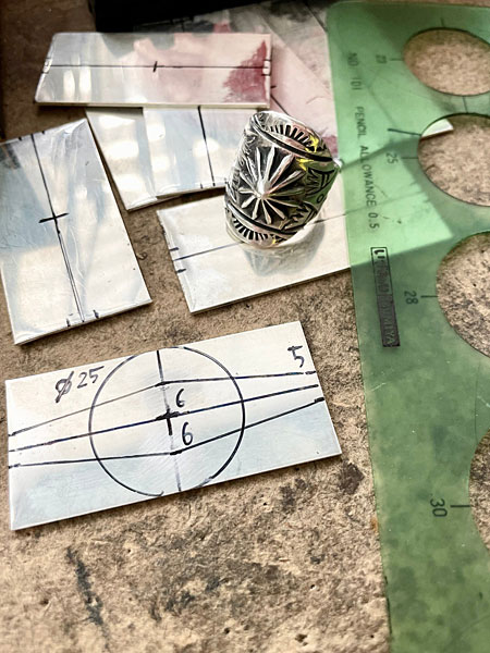 銀の板にラインが引かれ、これからリングへと成形される制作途中の工程がわかる画像。