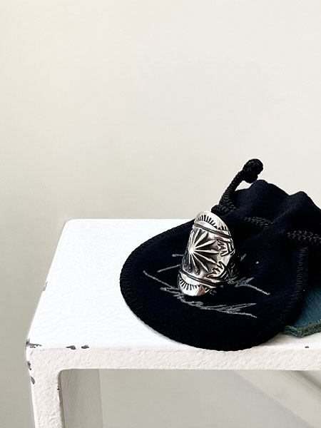 白い台の上に置かれたリングが、スタンプ模様とシルエットのバランスよく見えるディスプレイ画像。