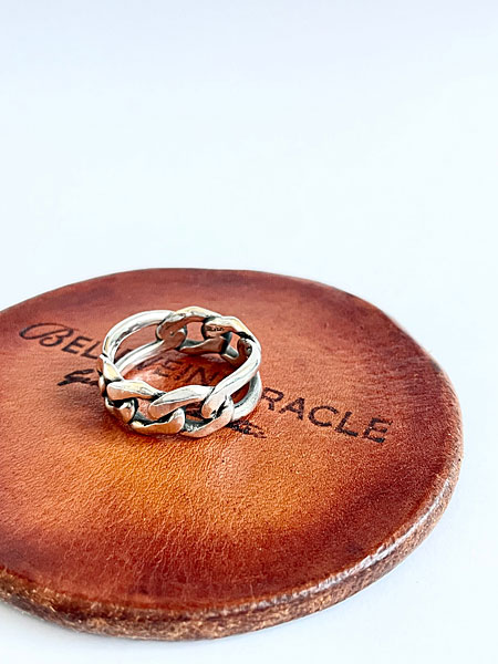 BELIEVEINMIRACLEの焼き印が押されたレザーの上にリングを置き、ブランドの世界観が感じられる画像。