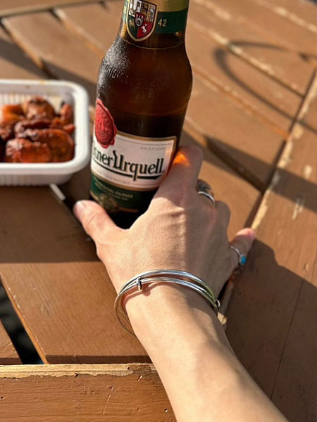 ビールを持った手元にワイヤーブレスレットを着用した、リラックスした雰囲気の着用画像。