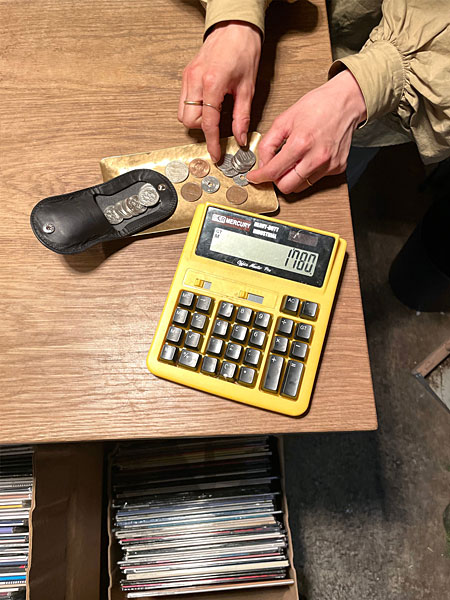 机の上で電卓やキャッシュトレーと一緒にコインケースを使用している、お会計シーンの様子を写した画像。