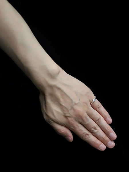 黒背景の中で男性の小指に自然に馴染む細身リングの着用イメージ画像。