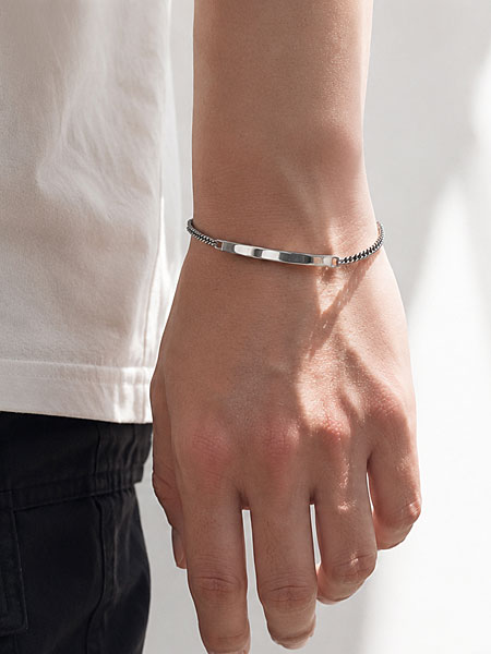 男性がIDブレスレットを着用し、華奢で上品なサイズ感がわかる手元の着用画像。