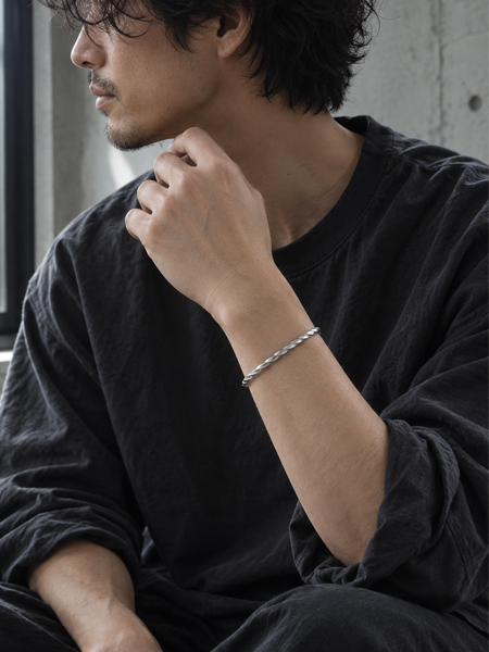 鏡面仕上げのつややかな輝きと立体的なツイストデザインが、男性の手元にスタイリッシュに馴染むバングルの着用画像。