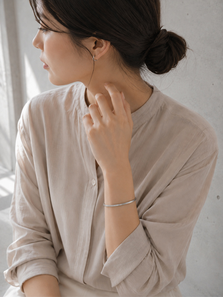 艶を抑えた細身のスクエアバングルが、シンプルな装いの女性の手元に上品ですっきりと馴染む着用画像。