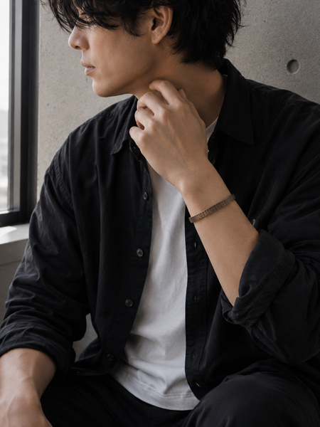 窓辺に立つモノトーンコーデの男性の手元に、程よい幅感とヴィンテージな質感が映えるバングルの着用画像。
