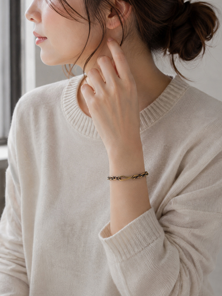 ヴィンテージ感のある真鍮製チェーンブレスレットが、女性の手元にほどよい存在感を添え、こなれた印象に馴染む着用画像。