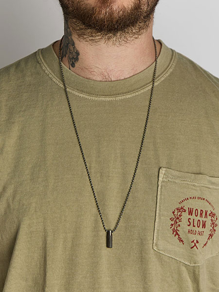 ロングシルエットのネックレスをカジュアルなTシャツに合わせ、胸元へさりげないアクセントを添えた男性の着用画像。