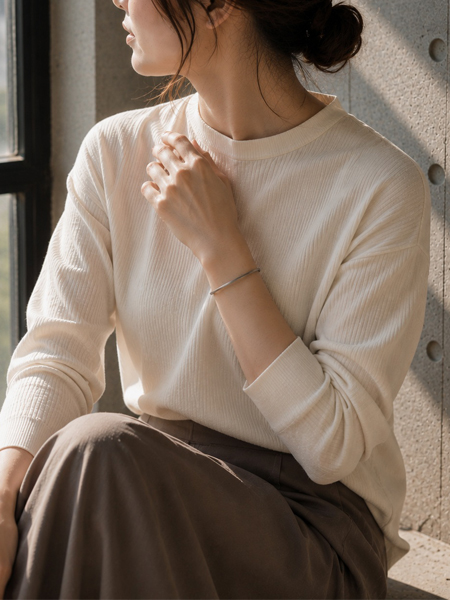やわらかなコーデの女性の腕元に、細身のバングルが上品に馴染む着用画像。