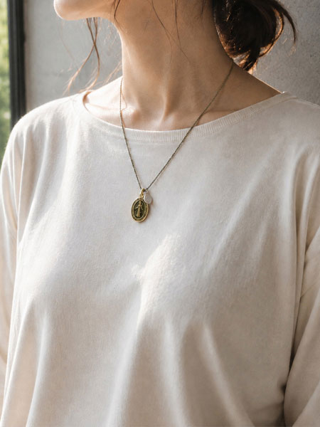 ベージュのトップスにマリアロケットネックレスを合わせた女性の着用画像。