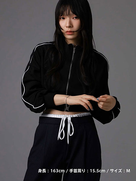 黒いジャージスタイルにシルバーチェーンブレスレットを合わせた女性の全身写真。