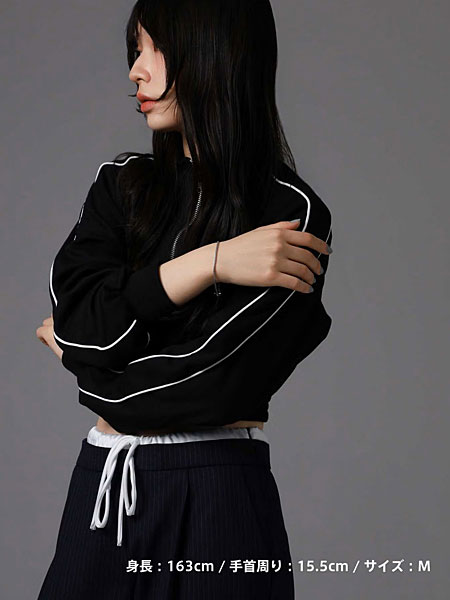 黒いジャージスタイルにシルバーチェーンブレスレットを合わせた女性の全身写真。