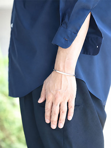 ネイビーシャツとスラックス風のパンツにカフバングルを合わせた男性の着用イメージ。