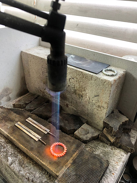 成形したリングに火を入れて、銀線の形を整えているアトリエでの制作シーン。