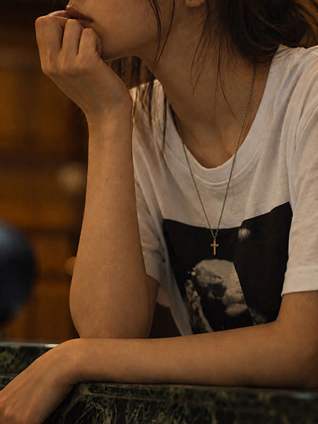 メンズライクなグラフィックTシャツにクロスネックレスを合わせた女性の胸元の着用画像。