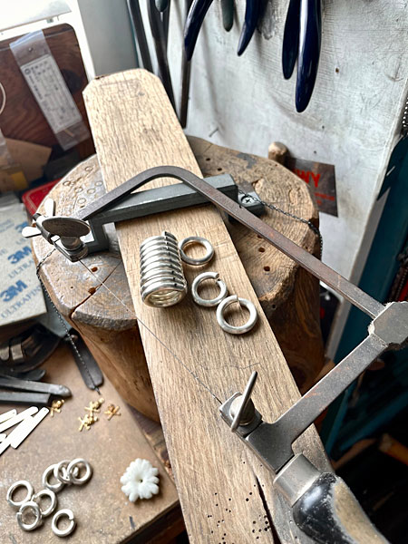 切り出されたリングとコイル状に形作られた銀線が作業台に並ぶ制作途中の画像。