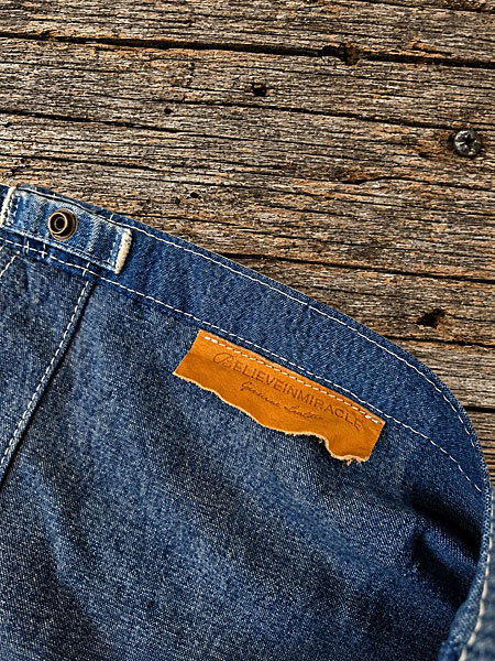 BELIEVEINMIRACLEとGenuine Leatherの文字が押印された、切りっぱなしのレザータグを縫い付けたディテール画像。