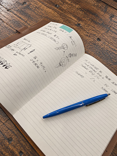 手帳カバーにセットしたメモ帳に文字が書かれ、そばにペンを置いた、日常での使用イメージが伝わる画像。