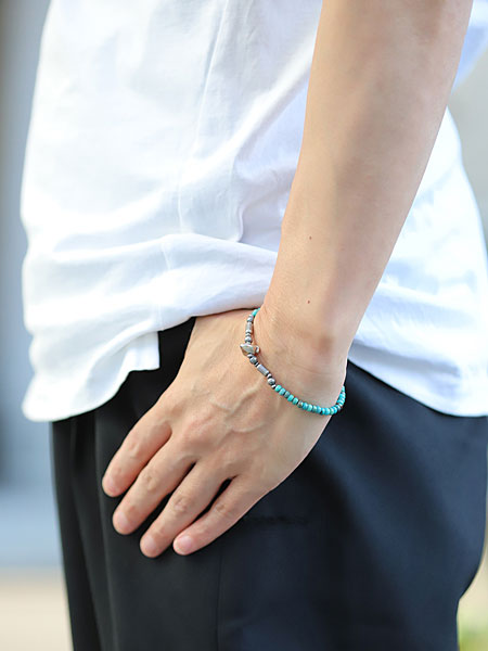 男性の手元を横から撮影した画像、ターコイズの濃淡とシルバーの輝きが自然に馴染み、シンプルな装いにマッチしている。