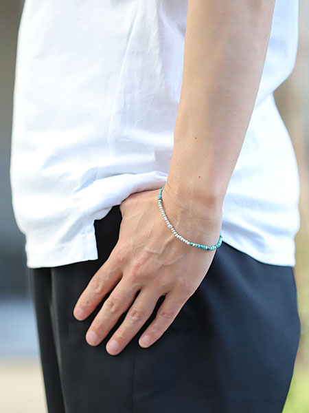 男性の手元を横から撮影した画像、ターコイズの濃淡とシルバーの輝きが自然に馴染み、シンプルな装いにマッチしている。