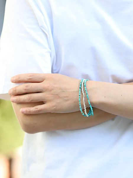 ターコイズネックレスを3連にしてブレスレットとして着用、重ね付けのような存在感で手元に華やかさをプラスしている。