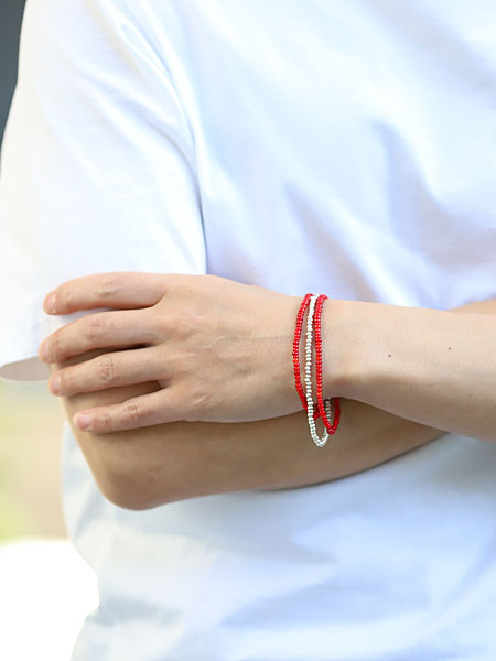 レッド ビーズ ネックレスを3連にしてブレスレットとして着用、重ね付けのような存在感で手元に華やかさをプラスしている。
