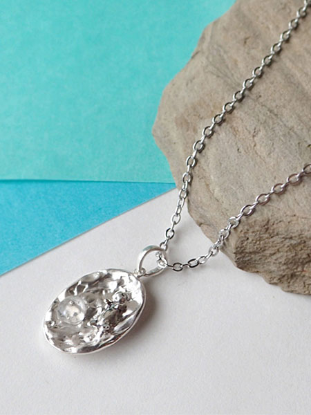 斜めから撮影したディスプレイ画像で、ラッコと水面モチーフの立体感が自然に伝わるペンダントトップのアップ画像。